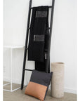 Walnut Black Yak With Hand Knotted Merino Stripes Handloom Throw displayed on a black ladder with a concrete vase and pillow.