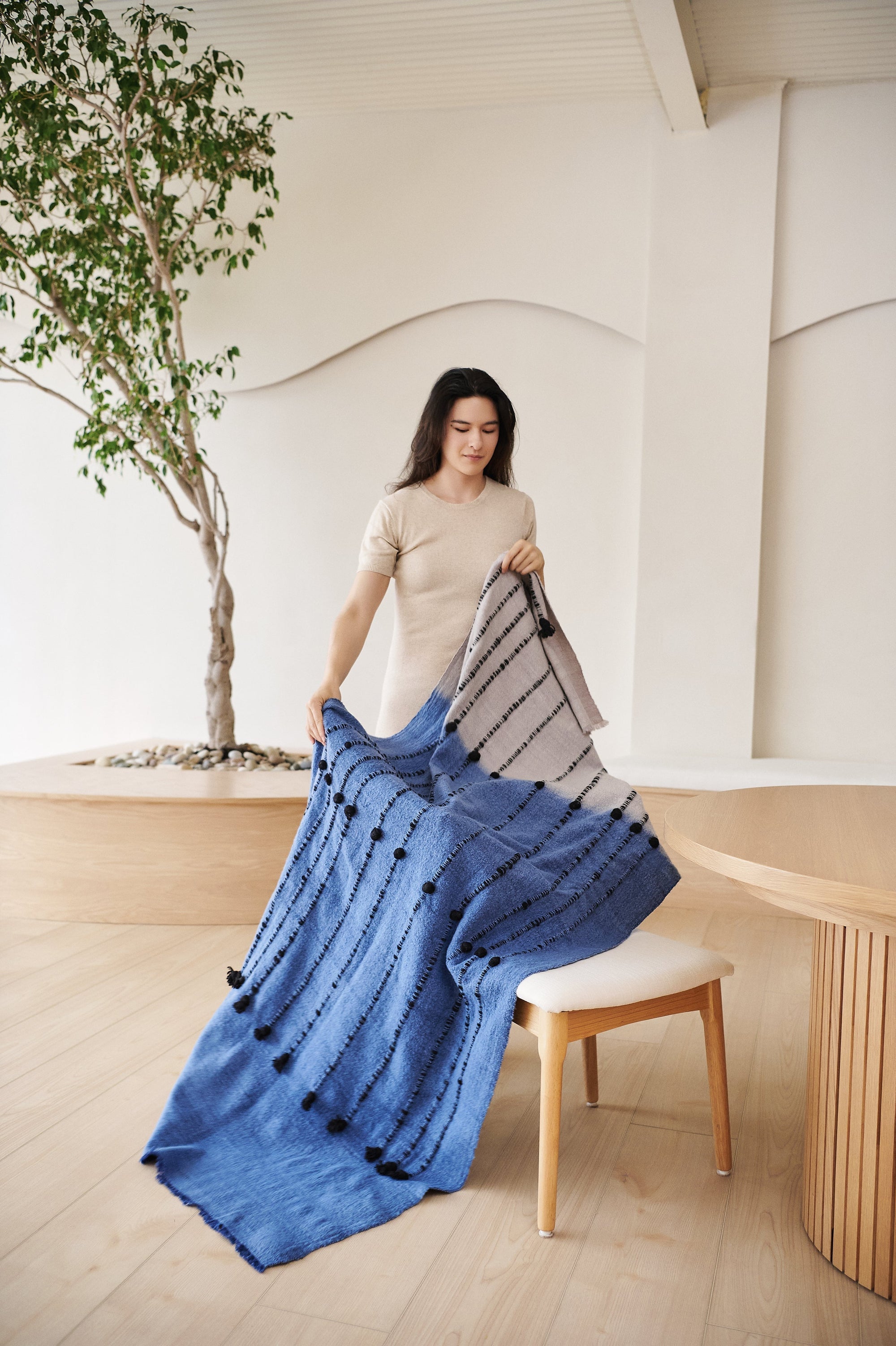 How to Style a Throw Blanket for Modern Interior Spaces with a woman arranging a blue and grey throw blanket.