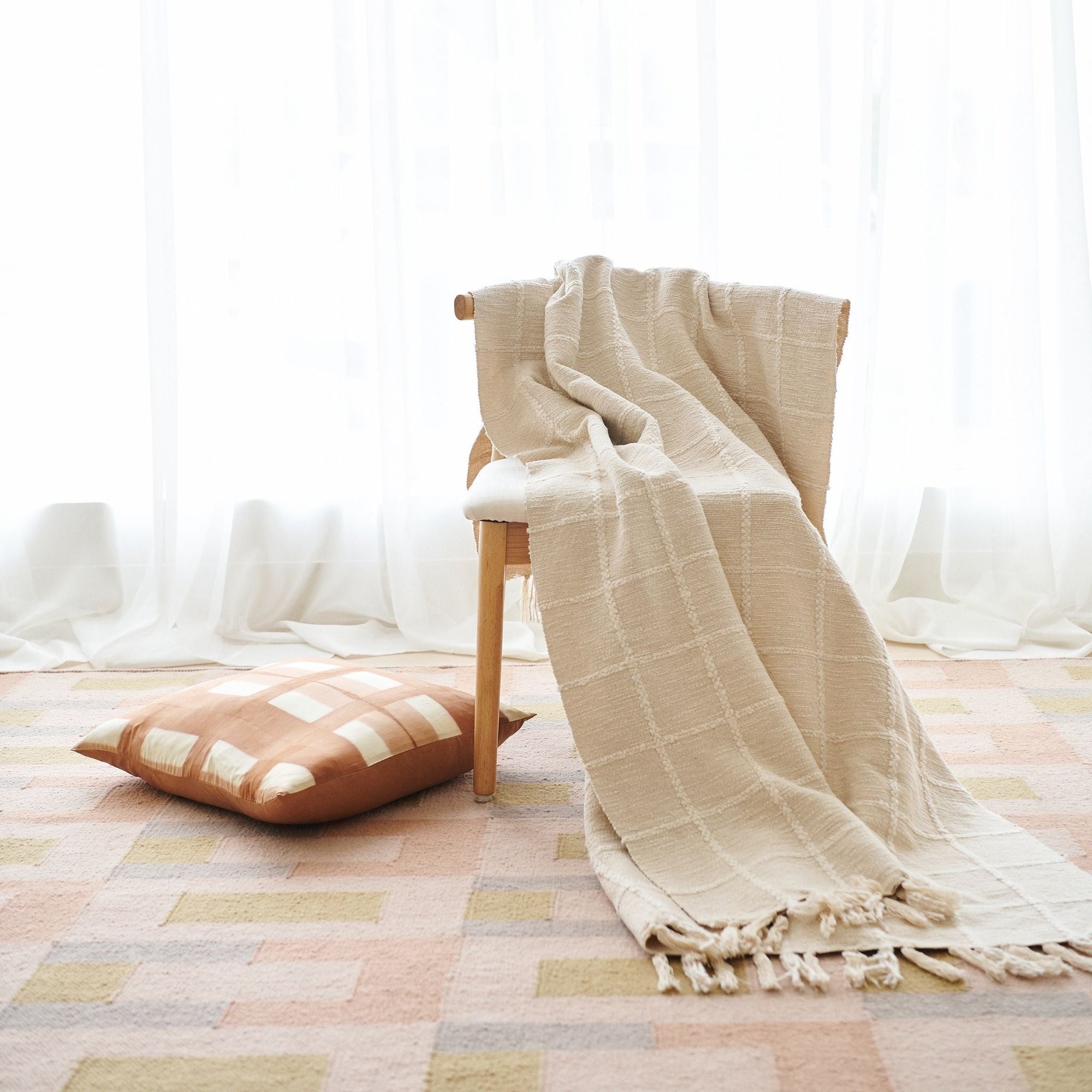 White throw styled on a chair with a gold silk pillow on the side laid on a rug