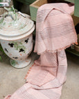 Silica Rose In Shades of Salmon Pink Gray Stripes Pattern Soft Handwoven Merino Throw displayed next to a decorative pot.