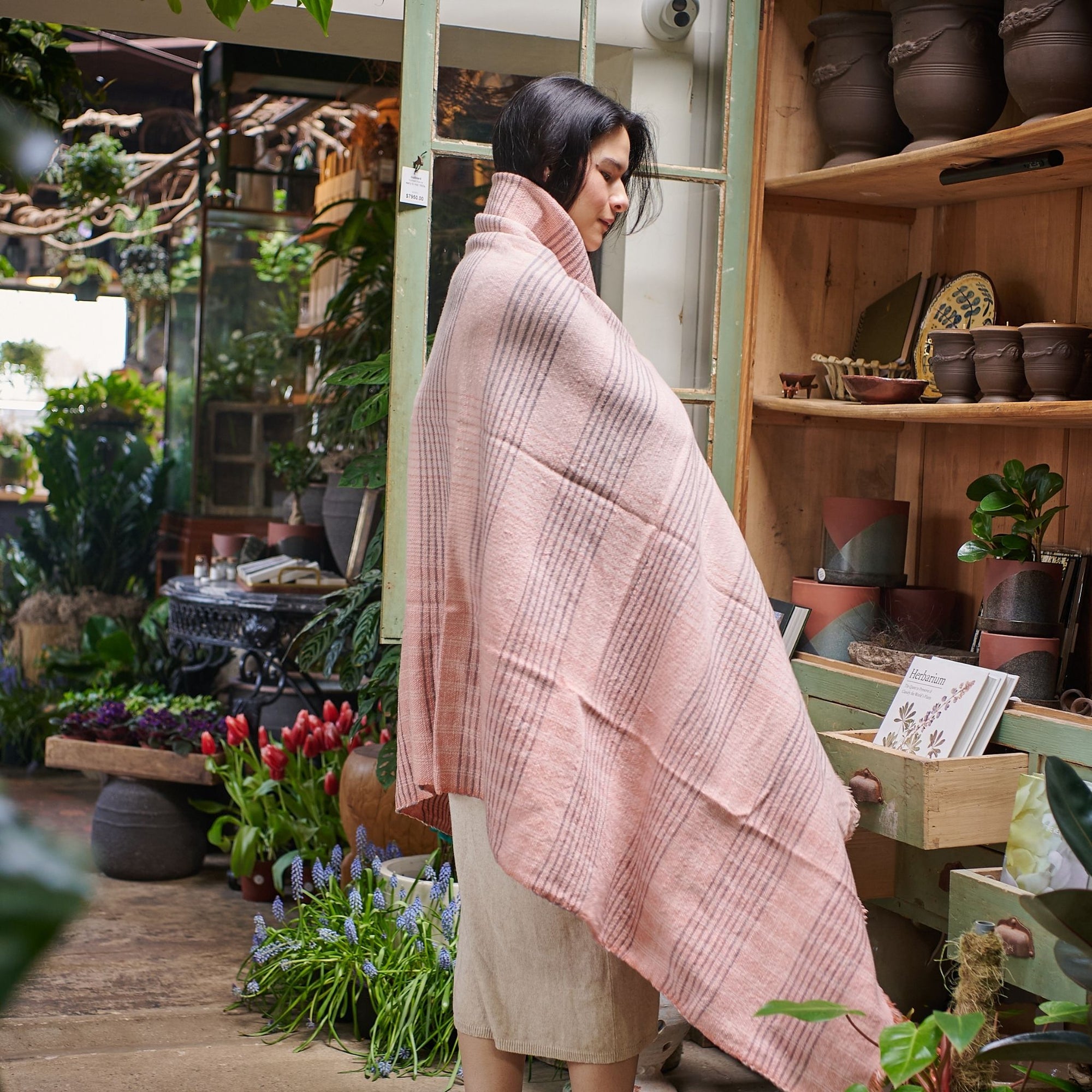 Silica Rose In Shades of Salmon Pink Gray Stripes Pattern Soft Handwoven Merino Throw wrapped around a model in a floral setting.