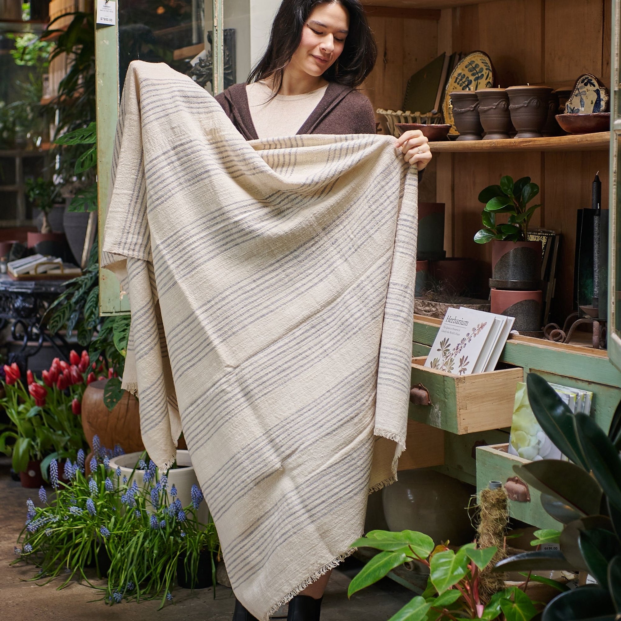 Silica Chalk Off White And Gray Stripes Pattern Soft Handwoven Merino Throw held by a woman in a botanical setting.