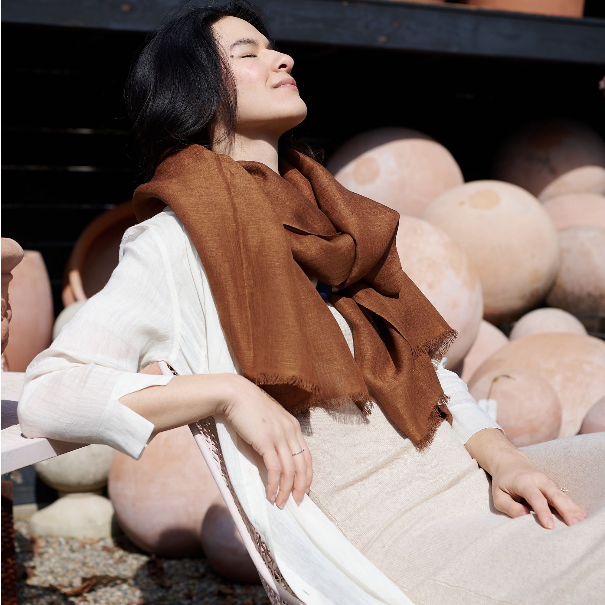 Woman wearing a Coco Brown Hand Woven Linen Silk Blend Scarf against a backdrop of pottery.