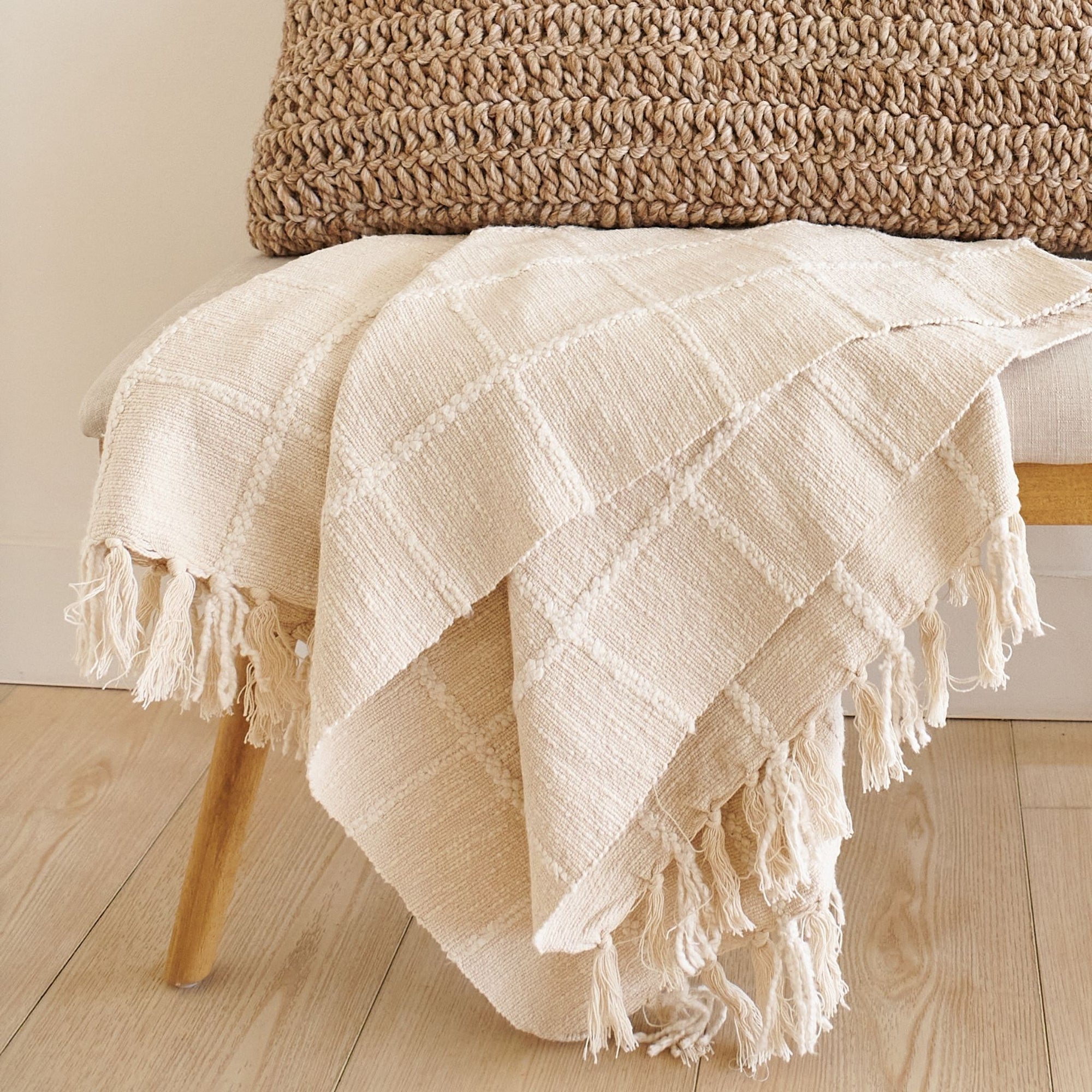Sea Shell White Textured Checks Handloom Throw displayed on a wooden bench, showcasing its elegant design and hand-rolled fringes.