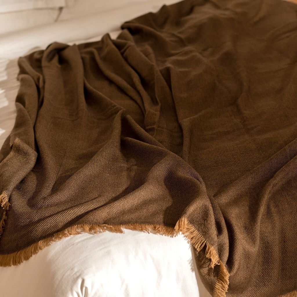 Hay Brown Twill Merino Handwoven Throw draped on a bed, showcasing its soft texture and elegant design.