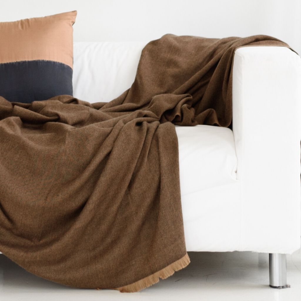 Hay Brown Twill Merino Handwoven Throw draped over a white sofa, showcasing its soft texture and rich color.