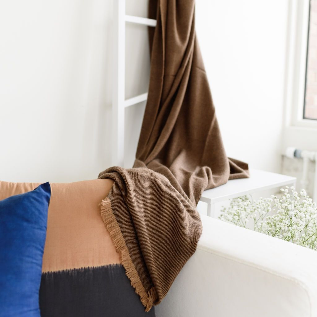 Hay Brown Twill Merino Handwoven Throw draped on a chair, showcasing its soft texture and subtle twill weave against decorative pillows.