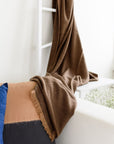 Hay Brown Twill Merino Handwoven Throw draped on a chair, showcasing its soft texture and subtle twill weave against decorative pillows.