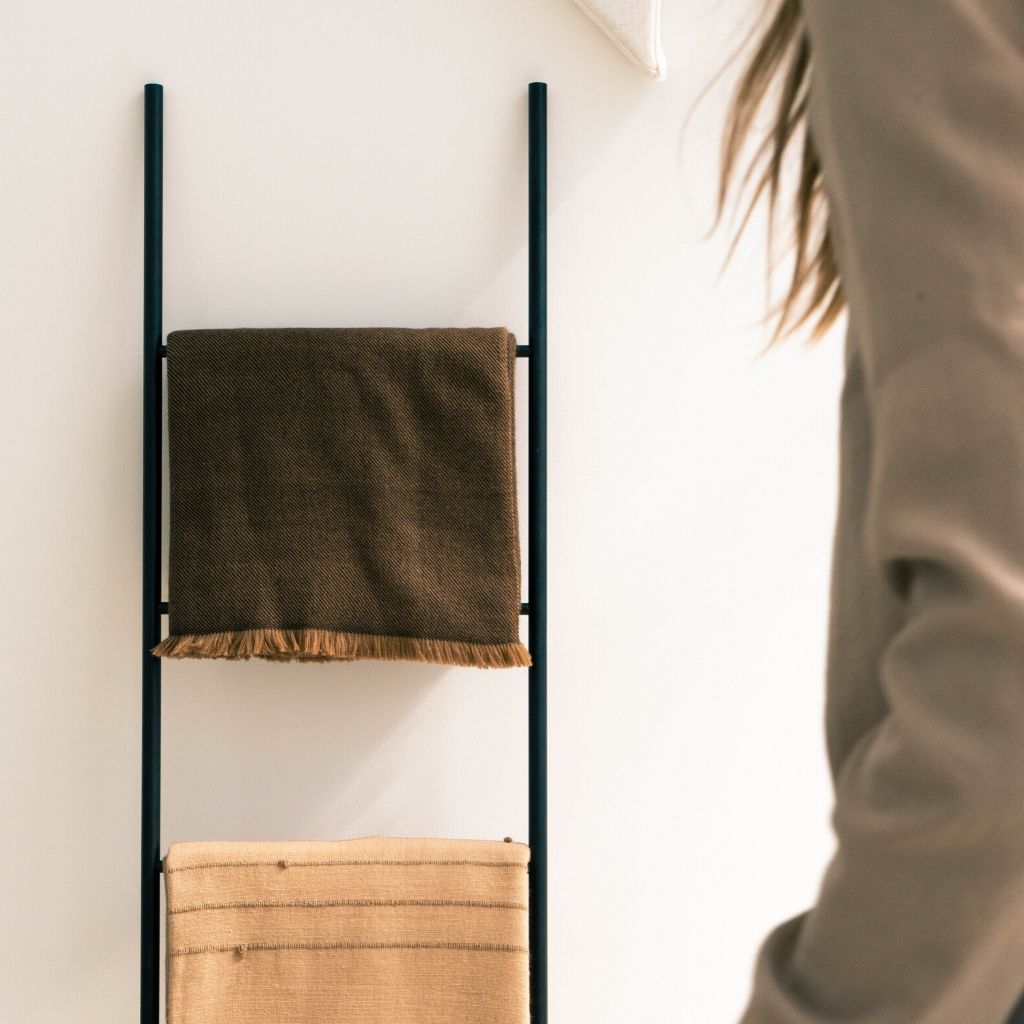 Hay Brown Twill Merino Handwoven Throw displayed on a wall ladder along with another blanket, showcasing its soft texture.