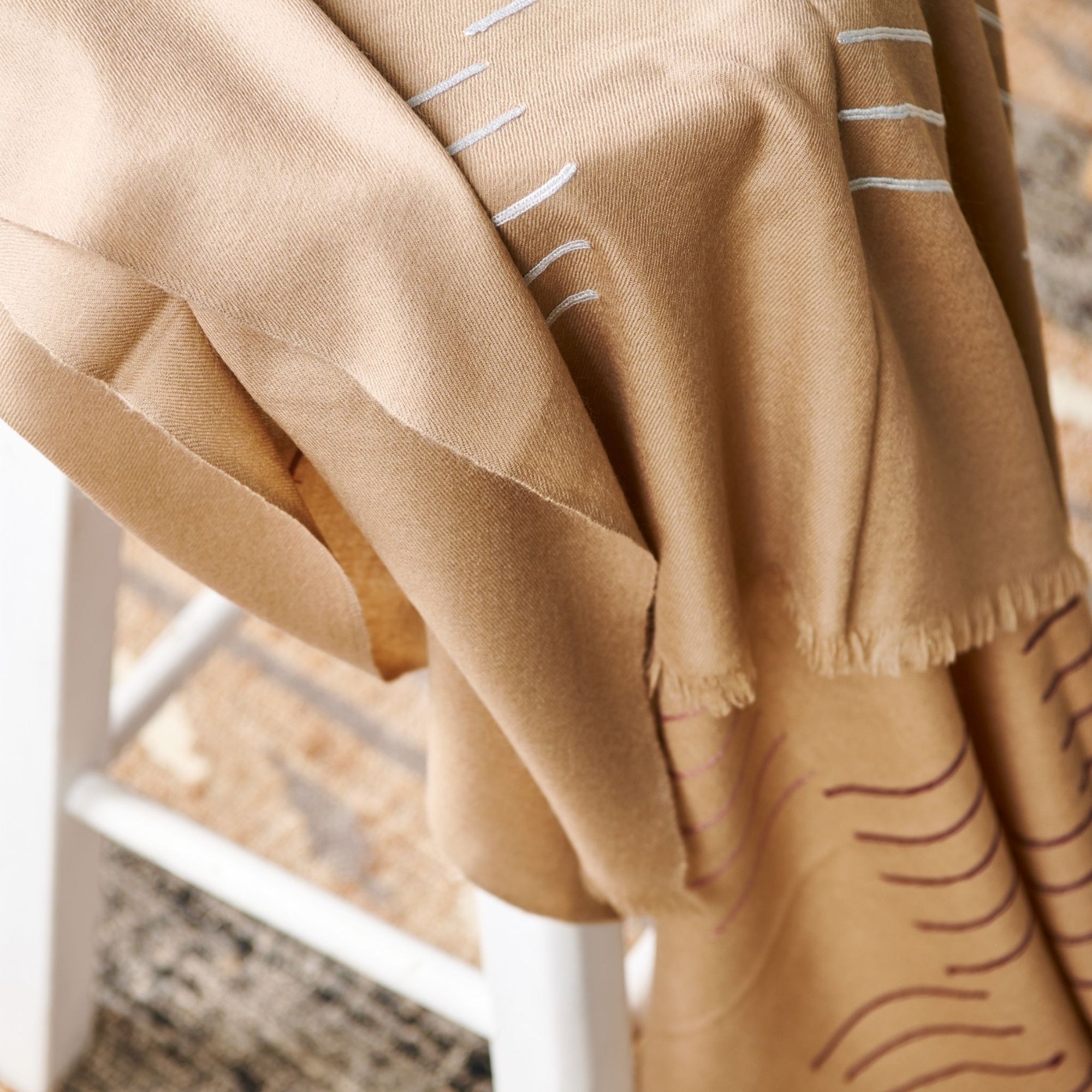 Maple Beige Handwoven Hand Embroidered Classic Scarf draped over a chair showcasing its soft texture and intricate design.