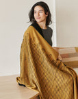 Handwoven Topaz Brown Myrtle Drift Merino Throw elegantly draped over a woman, showcasing its intricate design and texture.
