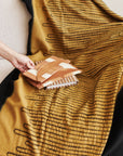 Handwoven Topaz Brown Myrtle Drift Merino Throw displayed on a couch with patterned cushions.