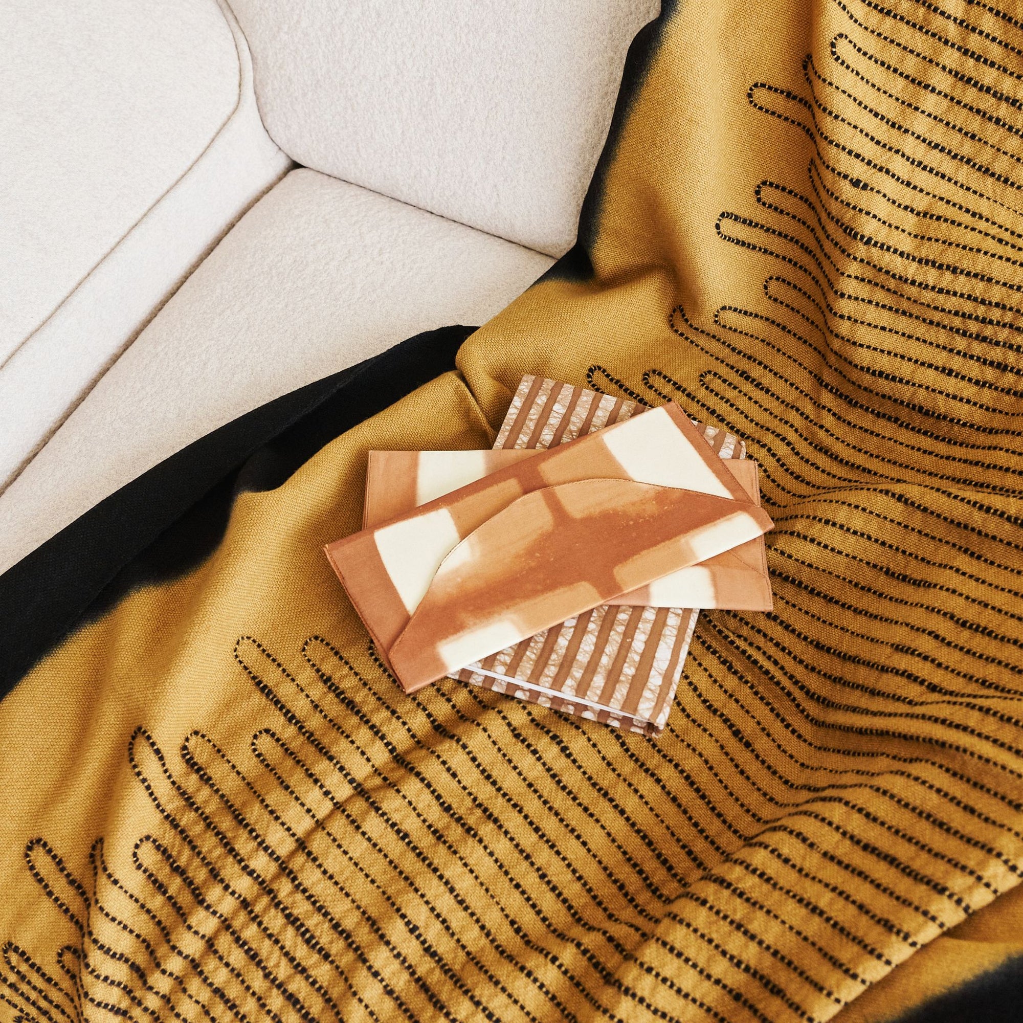 Handwoven Topaz Brown Myrtle Drift Merino Throw draped over a sofa with decorative coasters on top.