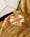 Handwoven Topaz Brown Myrtle Drift Merino Throw draped over a sofa with decorative coasters on top.