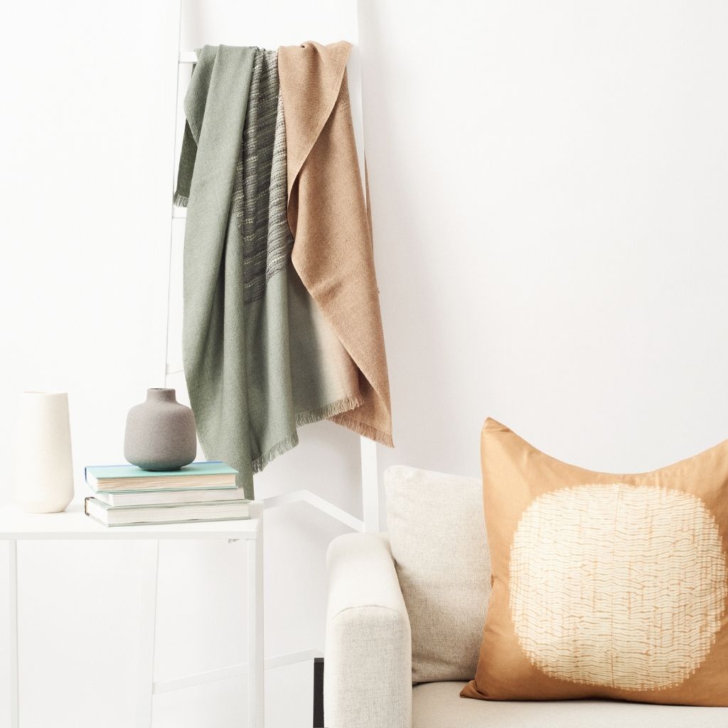 Salvia Green Brown Handwoven Merino Queen Size Bedspread styled on a white ladder with gold shunya silk pillow next to it on a white couch