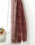 Auro Cinnabar Handwoven Earthy Rust Maroon Linen Scarf displayed on a ladder next to flowers.