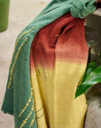 Avocado Green Multi Color Warm Hues Hand Woven Hand Knotted Textured Merino Throw draped over furniture with plants.