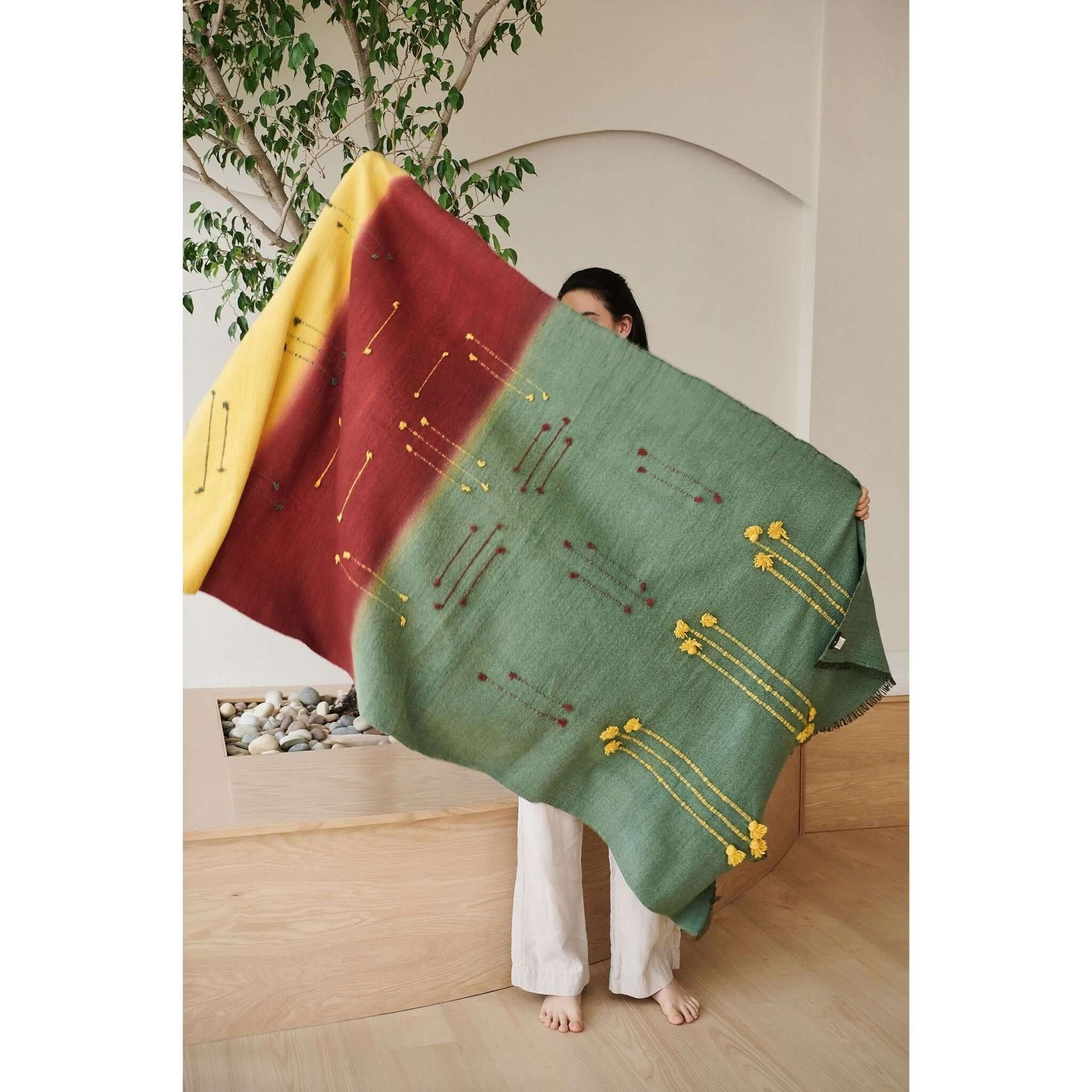 Avocado Green Multi Color Warm Hues Hand Woven Hand Knotted Textured Merino Throw displayed by a model indoors.