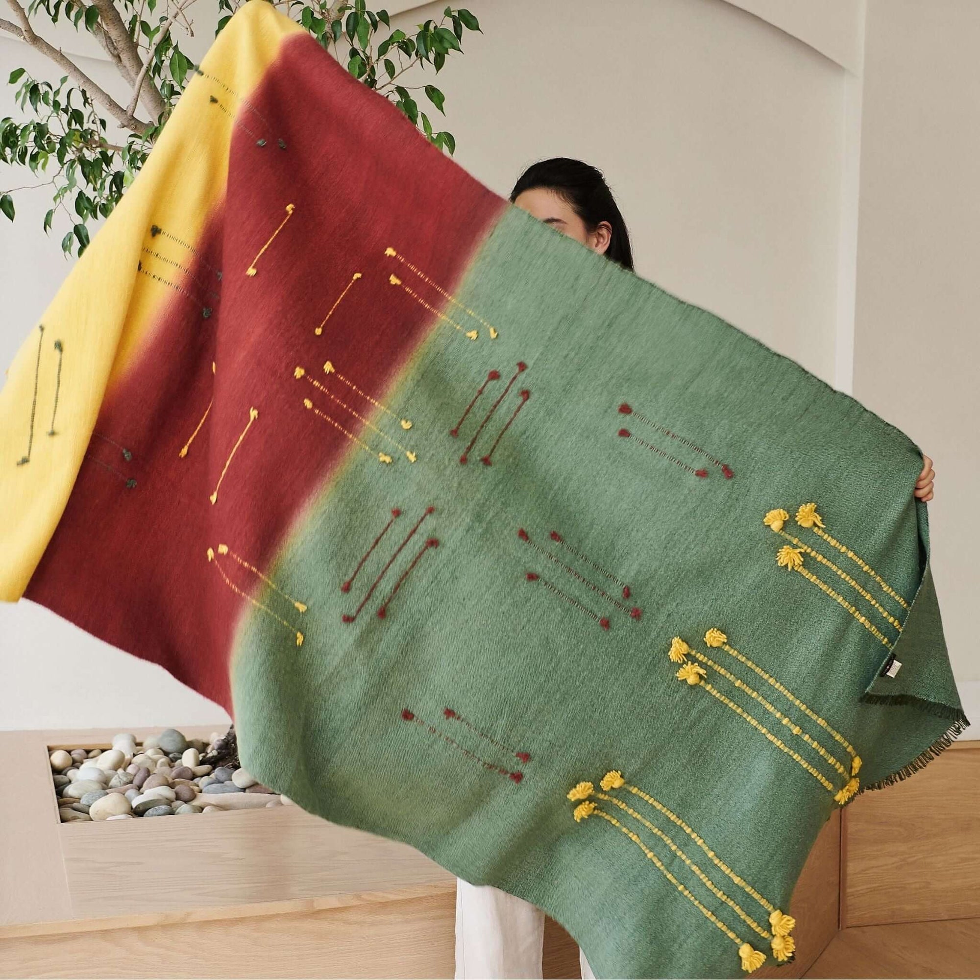 Avocado Green Multi Color Warm Hues Hand Woven Hand Knotted Textured Merino Throw draped elegantly by a person.