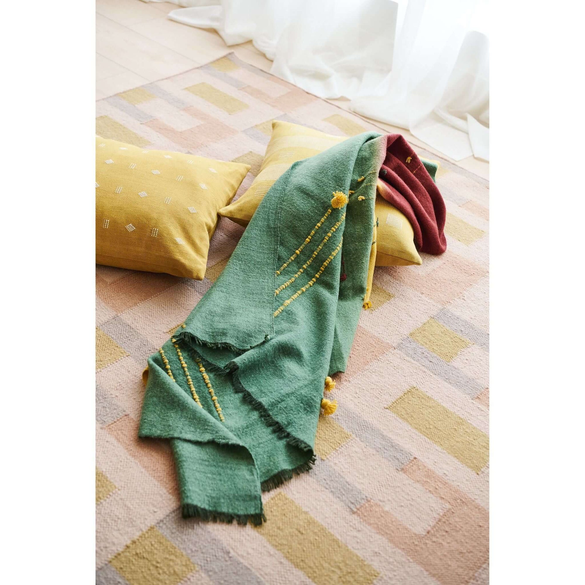 Avocado Green Multi Color Warm Hues Hand Woven Hand Knotted Textured Merino Throw draped over pillows on a soft rug.