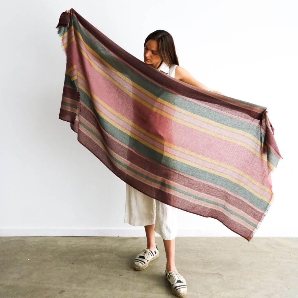 Woman holding the Barque Clay Modern Artisan Striped Soft Merino Handwoven Scarf against a white background.