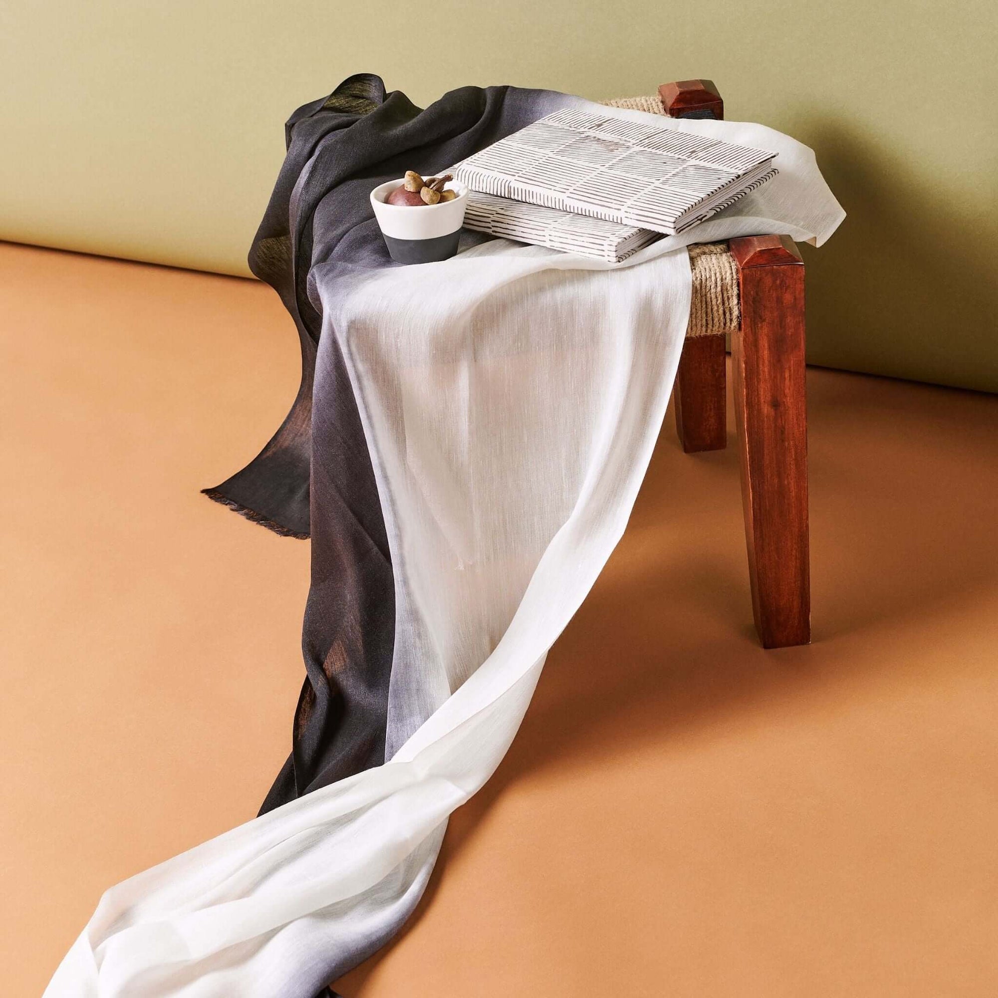 Bistre Black Zero Waste Handmade Artisanal Journal placed on a wooden stool with draped fabric and a small bowl.