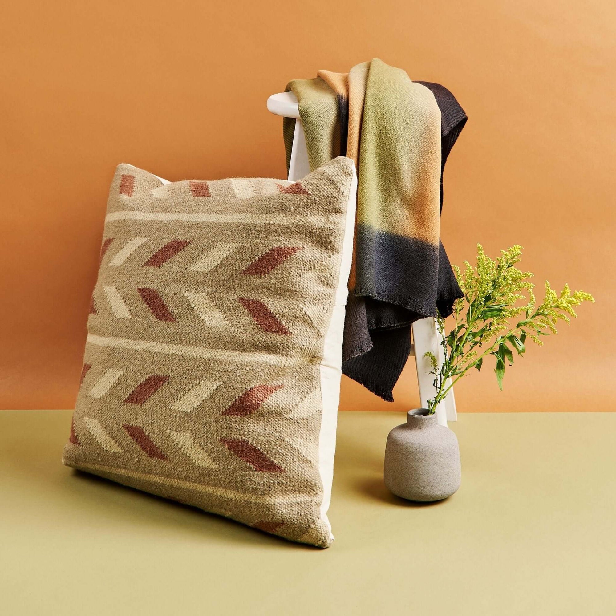 Ero Green Brown Geometric Pattern Hand Woven Large Pillow displayed with a blanket and vase on a stool.