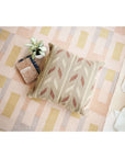 Ero Green Brown Geometric Pattern Hand Woven Large Pillow displayed on a textured area rug with a plant and books.