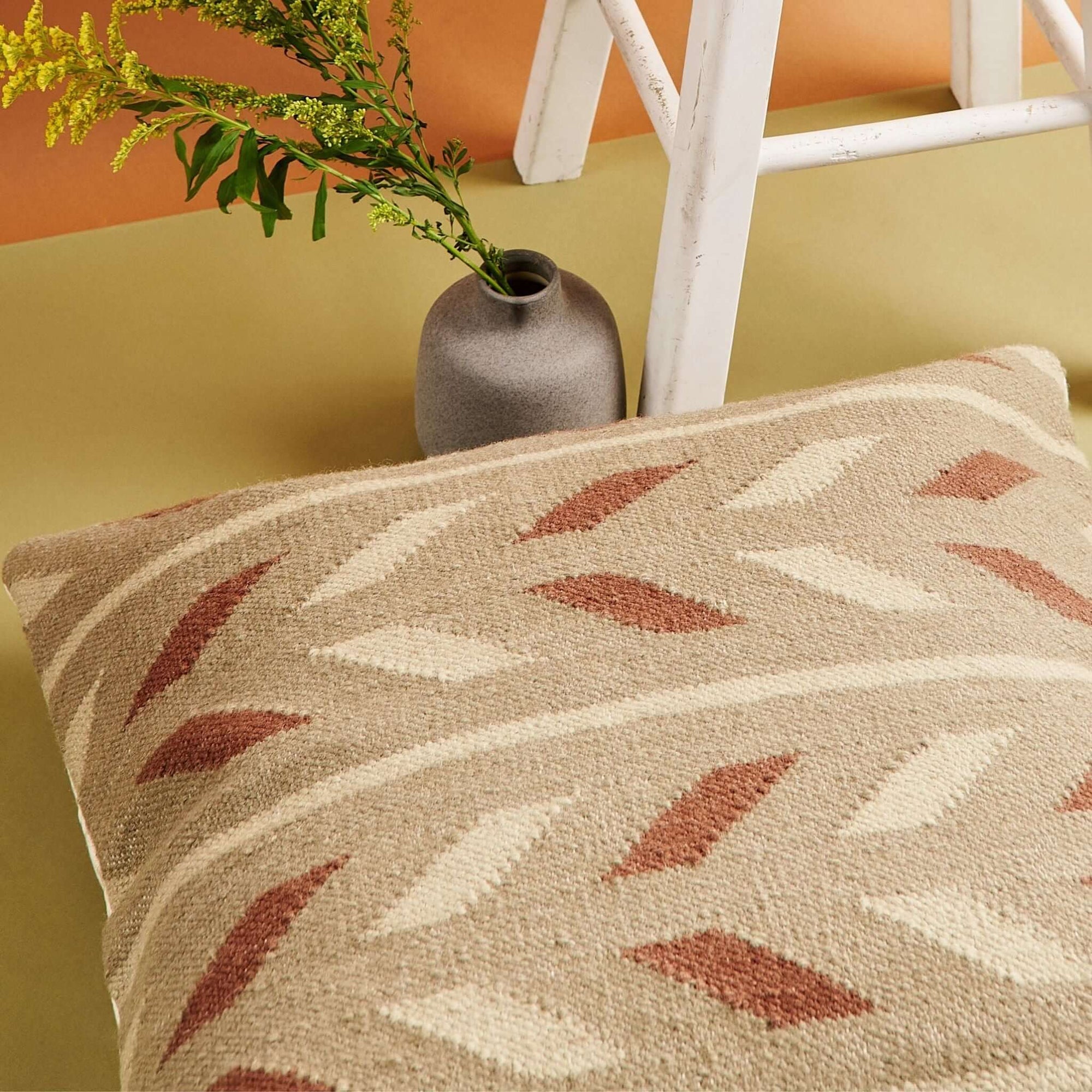 Ero Green Brown Geometric Pattern Hand Woven Large Pillow on a floor with a vase and plant in the background.