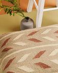Ero Green Brown Geometric Pattern Hand Woven Large Pillow on a floor with a vase and plant in the background.