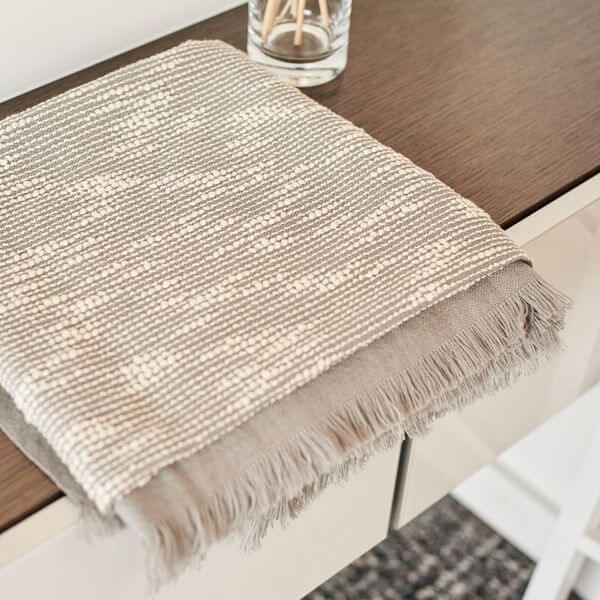 Flo Gray Textured Handloom Merino Throw displayed on a wooden surface, showcasing its luxurious design and craftsmanship.