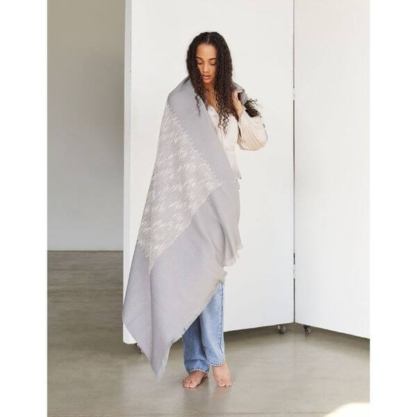 Flo Gray Textured Handloom Merino Throw draped elegantly by a woman in a spacious room.