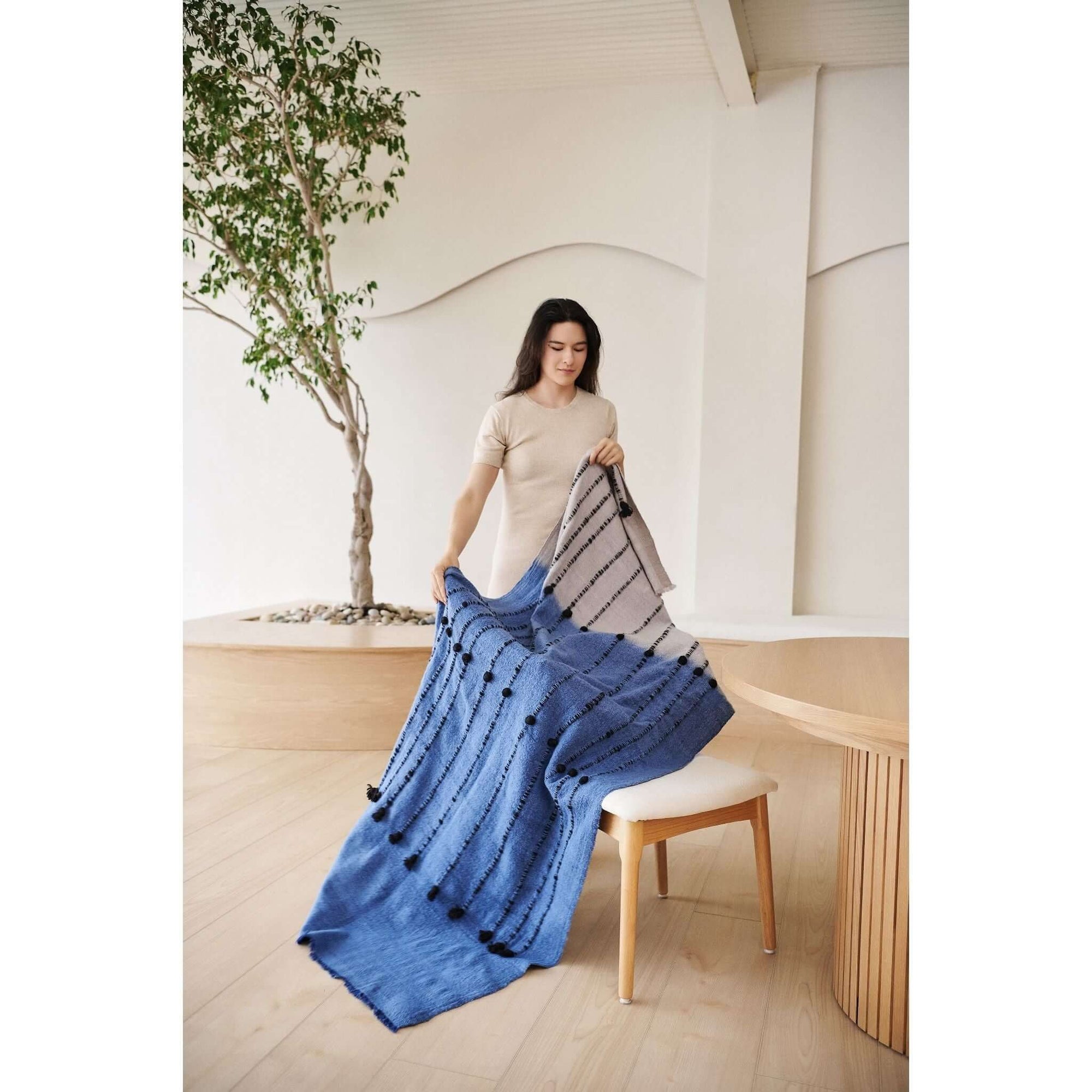 Hand Knotted Merino Textured Mari Throw Blanket in Blue Gray displayed by a woman in a modern interior.