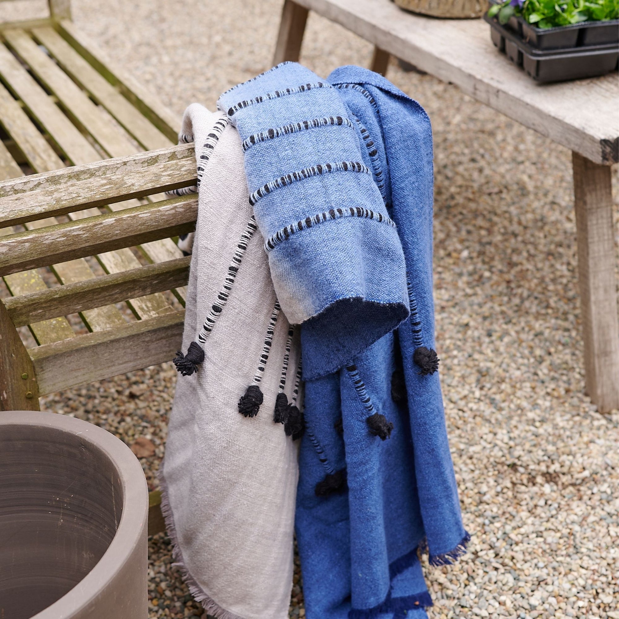 Hand Knotted Merino Textured Mari Throw Blanket in Blue Gray displayed on a wooden bench outdoors.