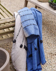 Hand Knotted Merino Textured Mari Throw Blanket in Blue Gray displayed on a wooden bench outdoors.