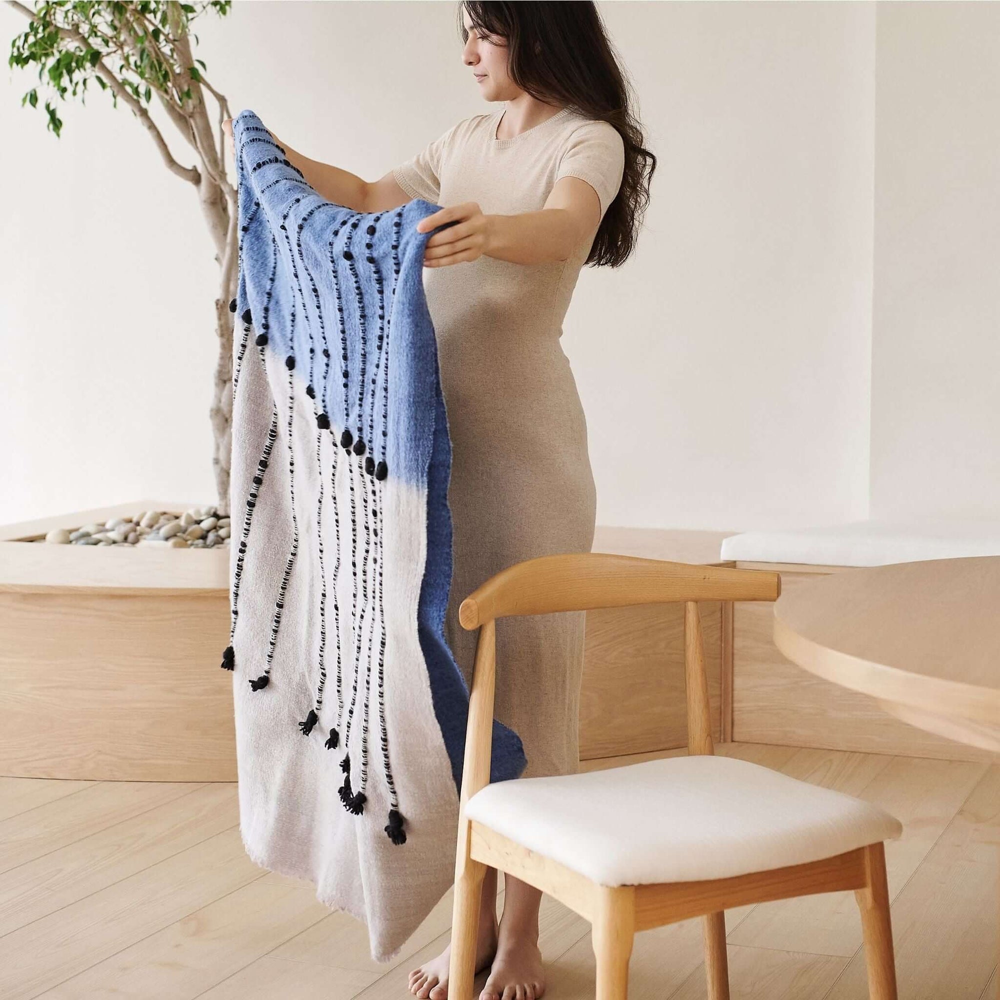 Hand Knotted Merino Textured Mari Throw Blanket in Blue Gray held by a woman in a serene indoor setting.