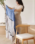 Hand Knotted Merino Textured Mari Throw Blanket in Blue Gray held by a woman in a serene indoor setting.
