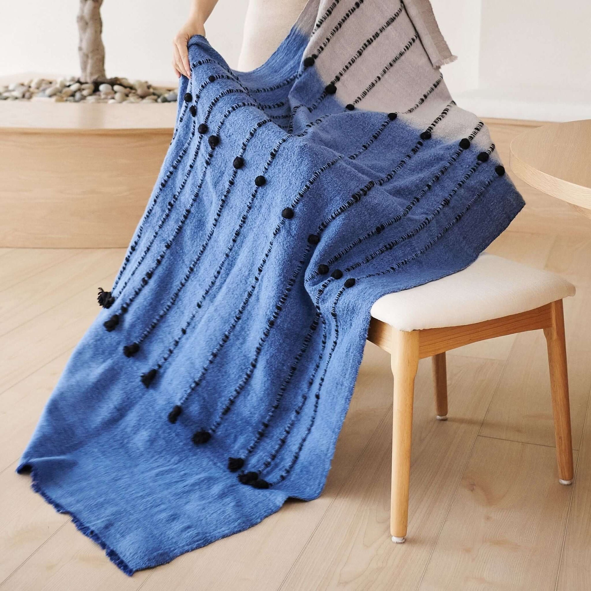 Hand Knotted Merino Textured Mari Throw Blanket in Blue Gray draped over a chair, showcasing its tactile texture and serene colors.