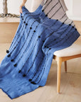 Hand Knotted Merino Textured Mari Throw Blanket in Blue Gray draped over a chair, showcasing its tactile texture and serene colors.