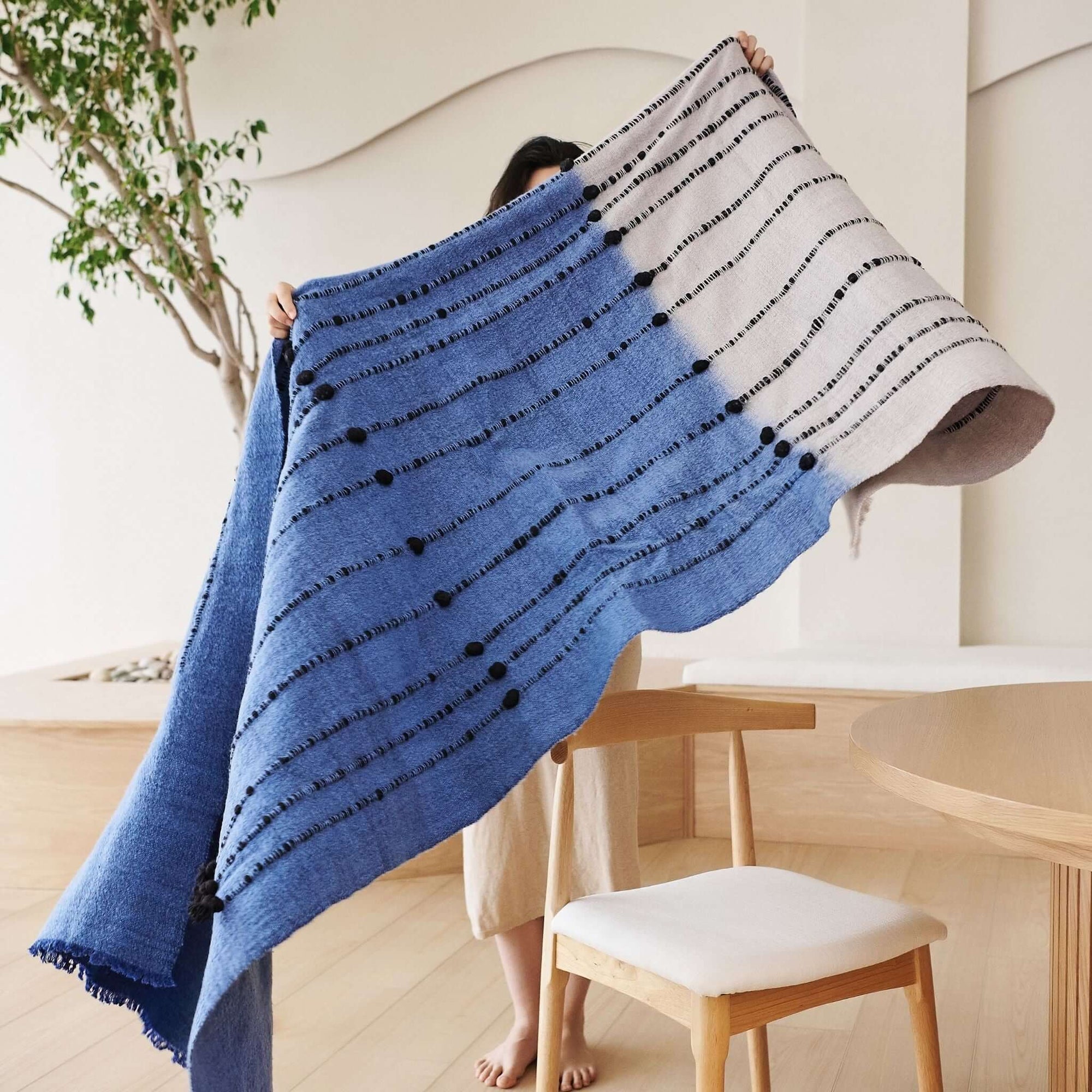 Hand Knotted Merino Textured Mari Throw Blanket in Blue Gray displayed elegantly by a person in a minimalist setting.
