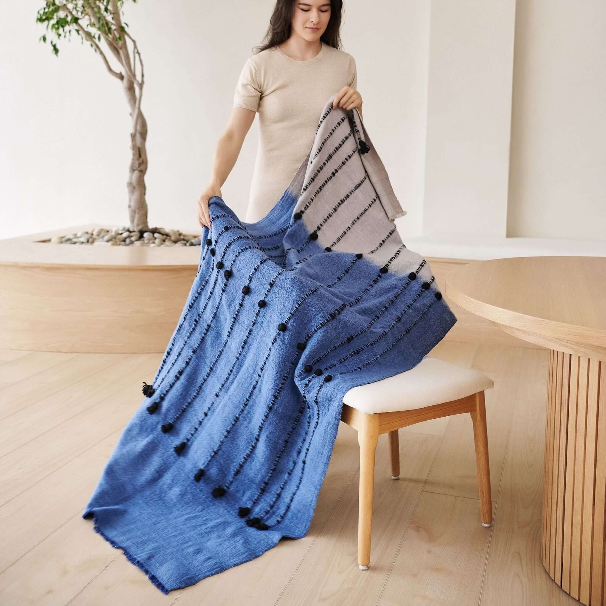 Hand Knotted Merino Textured Mari Throw Blanket in Blue Gray displayed by a model in a cozy interior setting.