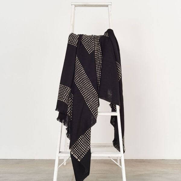 Walnut Black Yak With Hand Knotted Merino Stripes Handloom Throw displayed on a ladder, featuring black with dotted stripes.