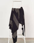 Walnut Black Yak With Hand Knotted Merino Stripes Handloom Throw displayed on a ladder, featuring black with dotted stripes.