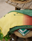 Avocado Green Multi Color Warm Hues Hand Woven Hand Knotted Textured Merino Throw displayed on a wooden table.