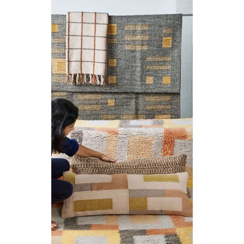 Person arranging Ash Blue Gray Jute Handwoven Geometric Pattern Rug and pillows in a cozy living room setting.