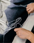 Person hand stitching the hem of the Ink Black White Ombre Textured Throw In Hand Spun Merino And Hand Stitched Hem.