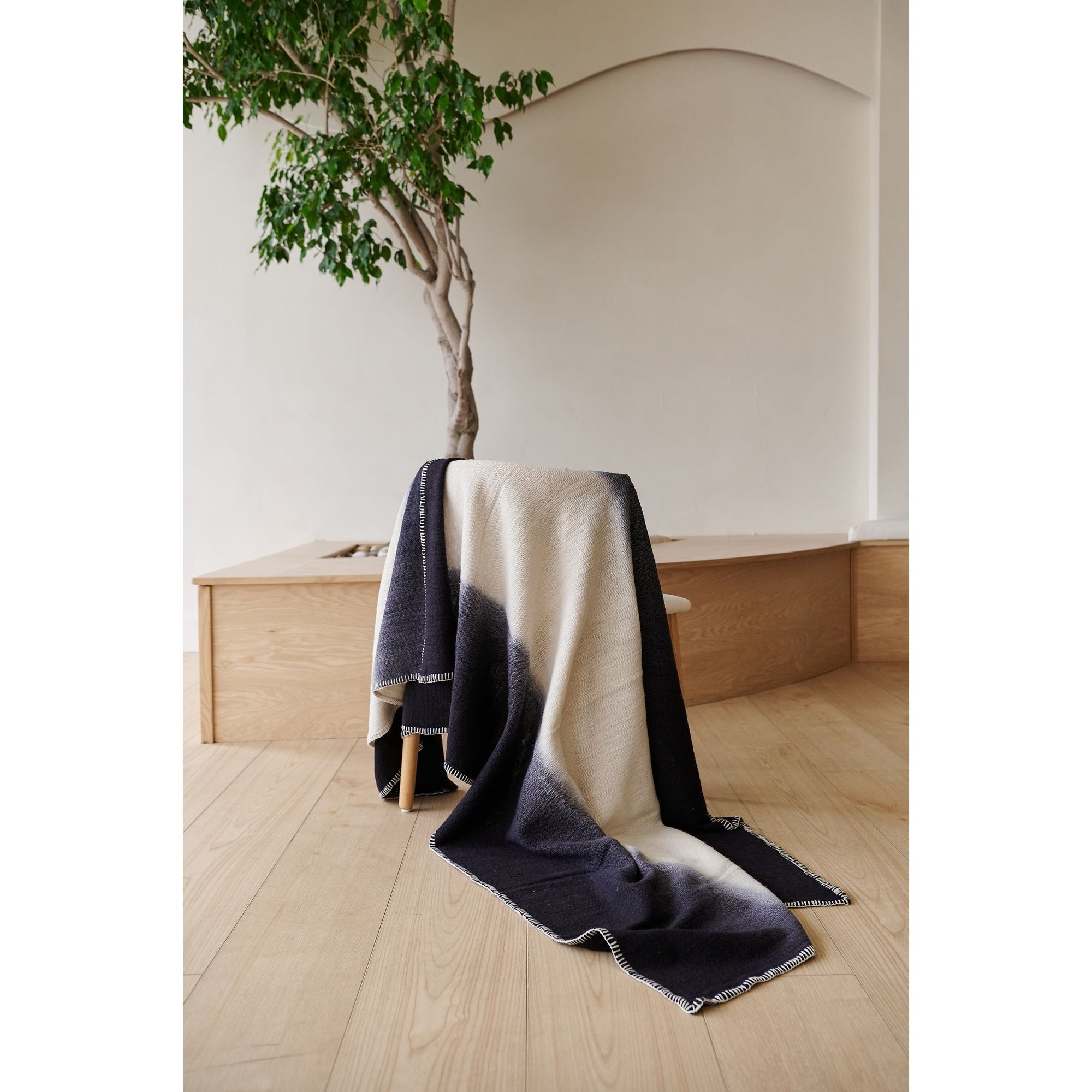 Ink Black White Ombre Textured Throw In Hand Spun Merino And Hand Stitched Hem draped on a chair in a bright room.