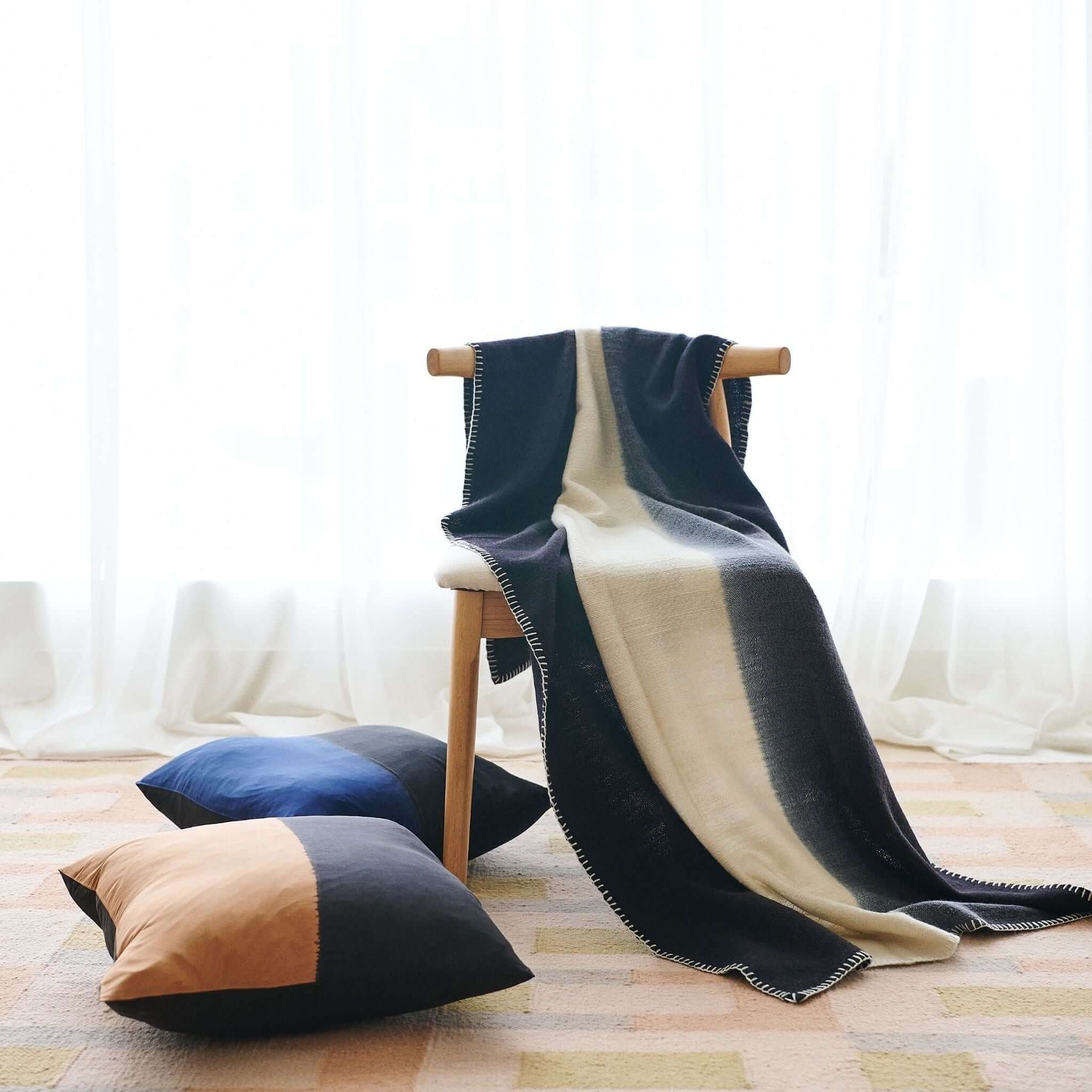 Ink Black White Ombre Textured Throw In Hand Spun Merino And Hand Stitched Hem draped over a chair with decorative pillows.