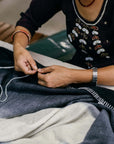 Artisan hand stitching the Ink Black White Ombre Textured Throw In Hand Spun Merino And Hand Stitched Hem.