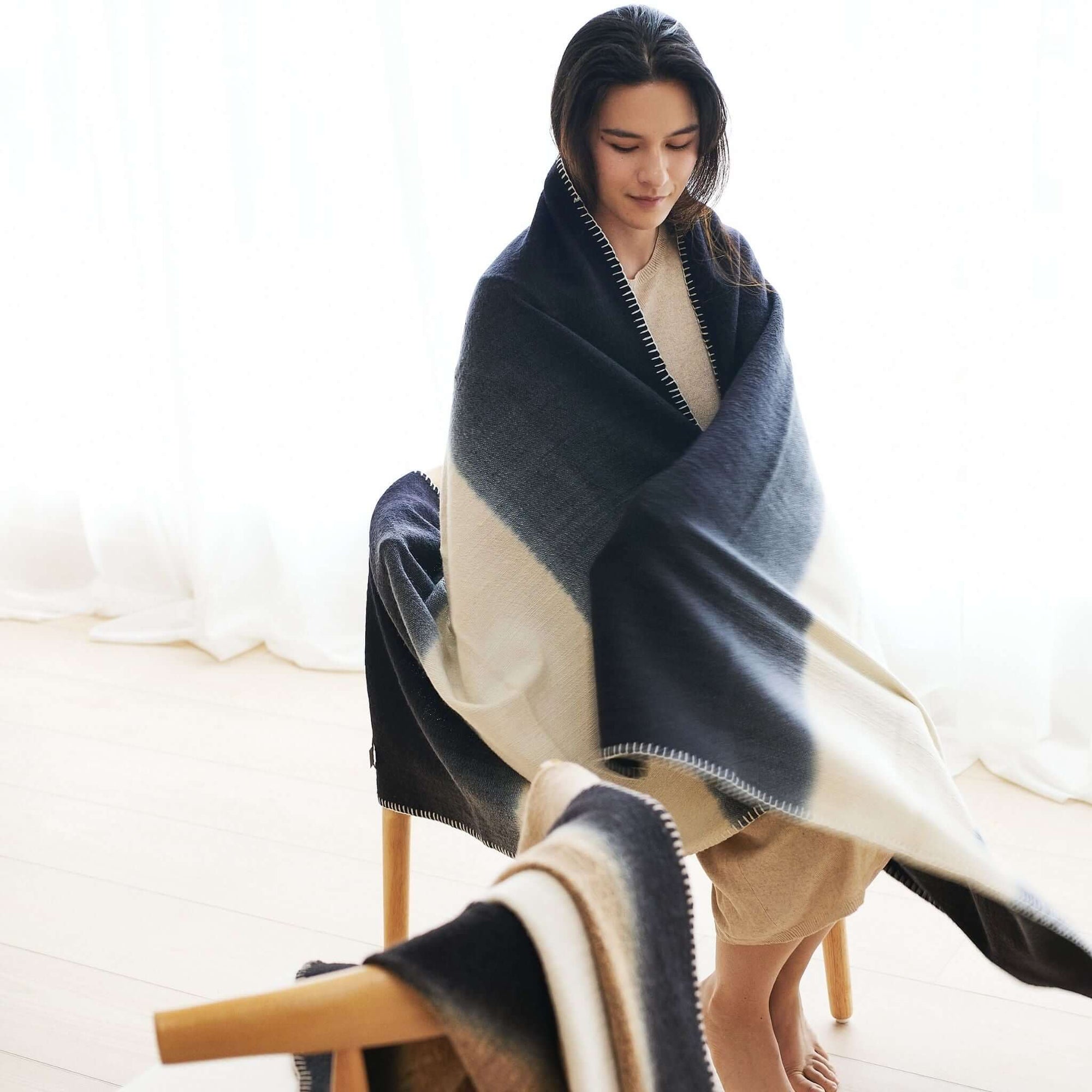 Ink Black White Ombre Textured Throw  In Hand Spun Merino And Hand Stitched Hem wrapped around a woman sitting.